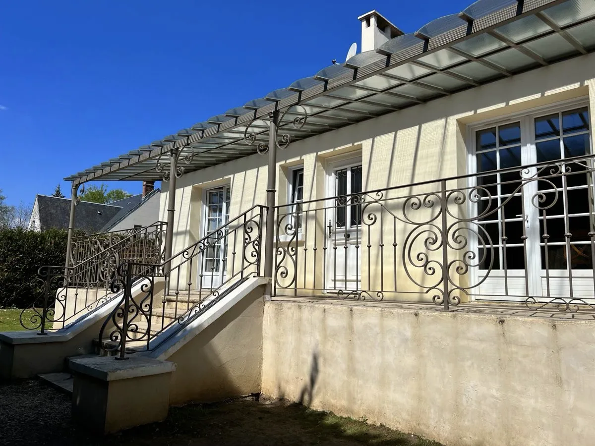 Pergola adossée en fer forgé gris beige sur maison en pierre, couverture verre armé petite maille, volutes forgées, Saint-Jean-aux-Bois, L'Art de Faire