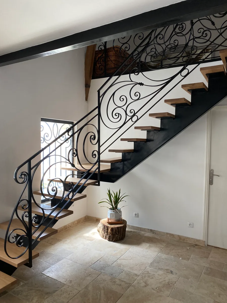 Escalier tournant en fer forgé à volutes, rampe ouvragée le long d'un mur en pierre, L'Art de Faire