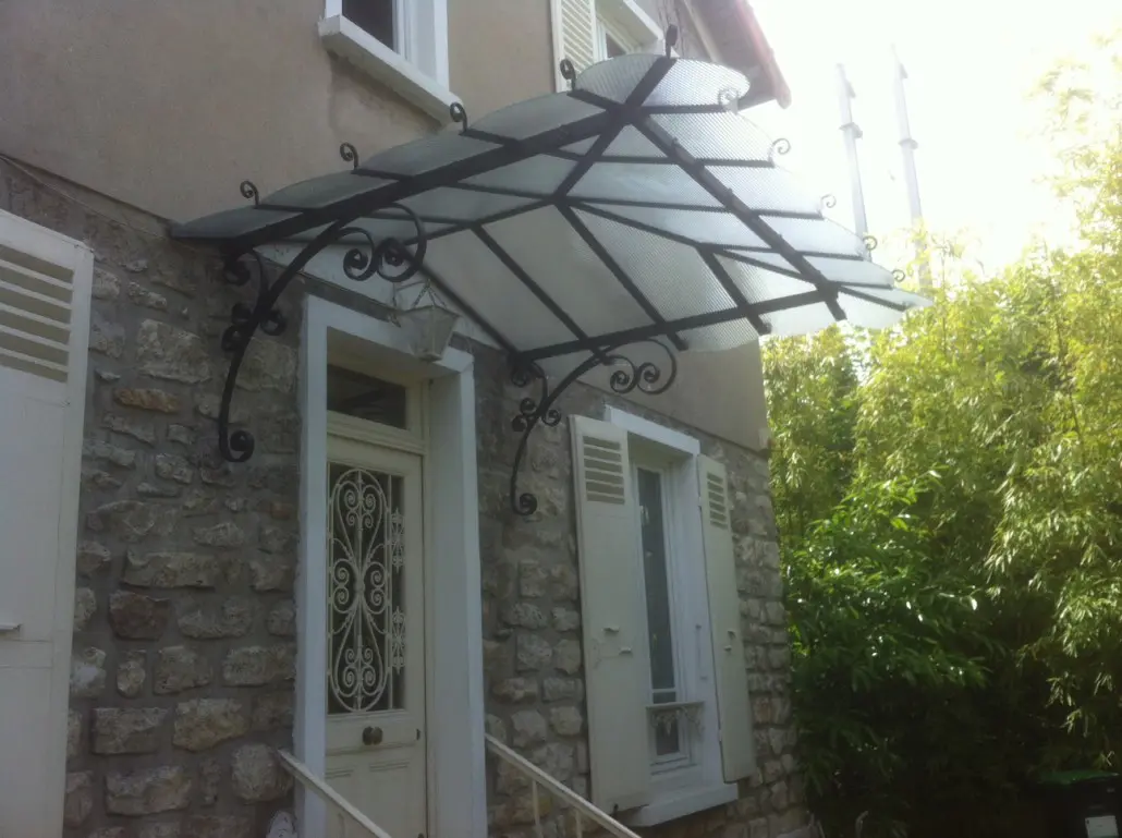 Grande marquise patrimoniale en fer forgé à volutes et toit vitré sur demeure en pierre, L'Art de Faire