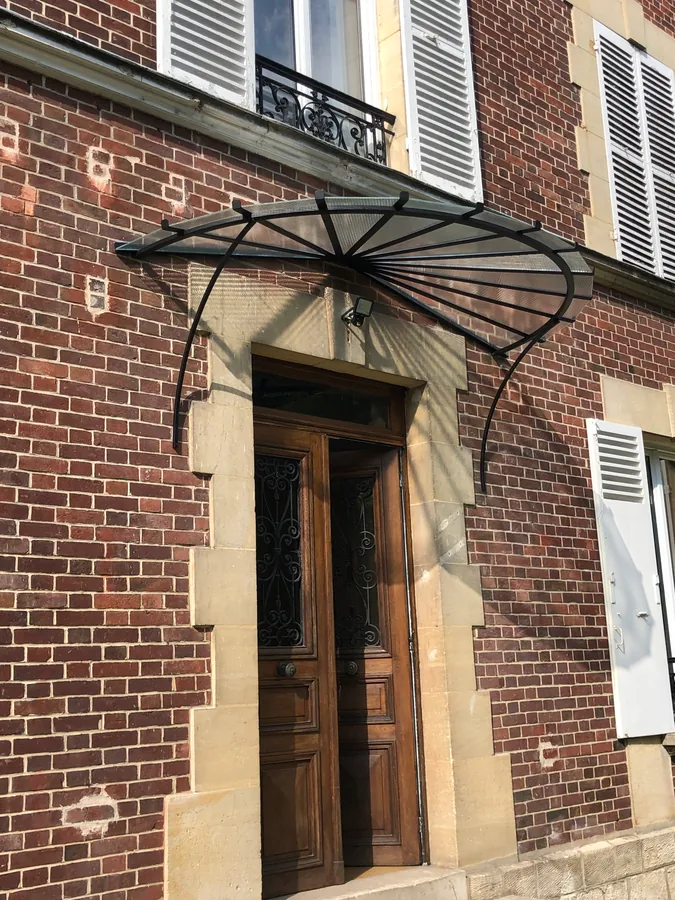 Marquise en fer forgé au-dessus d'une porte d'entrée sur façade en brique, L'Art de Faire