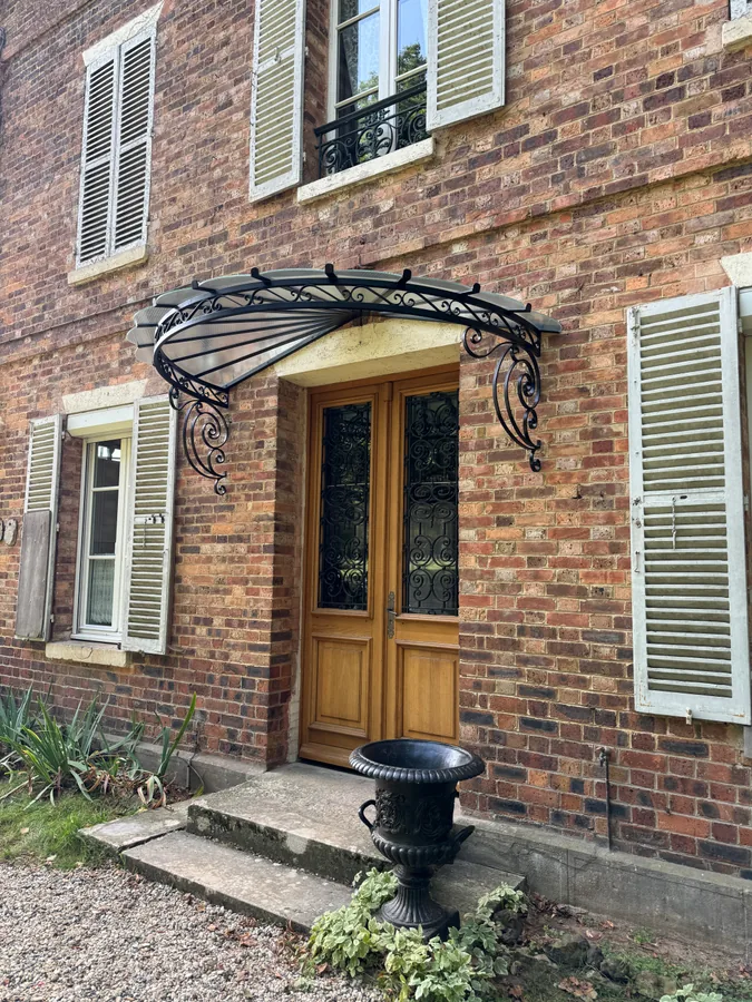 Marquise en fer forgé au-dessus d'une porte en bois sur façade en brique, L'Art de Faire