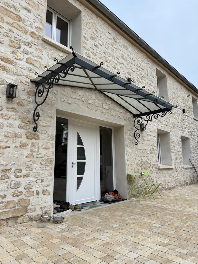 Marquise en fer forgé au-dessus d'une porte cintrée, maison en pierre, L'Art de Faire