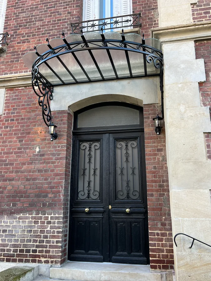 Marquise cintrée en fer forgé au-dessus d'une porte d'entrée en arc, L'Art de Faire