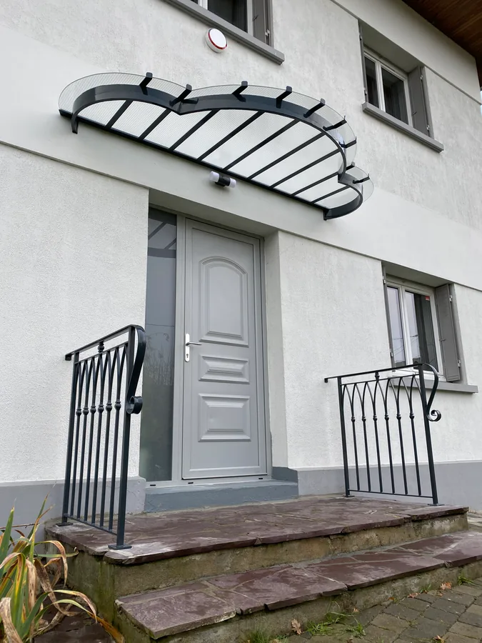Marquise en fer forgé et verre au-dessus d'une porte blanche, maison contemporaine, L'Art de Faire