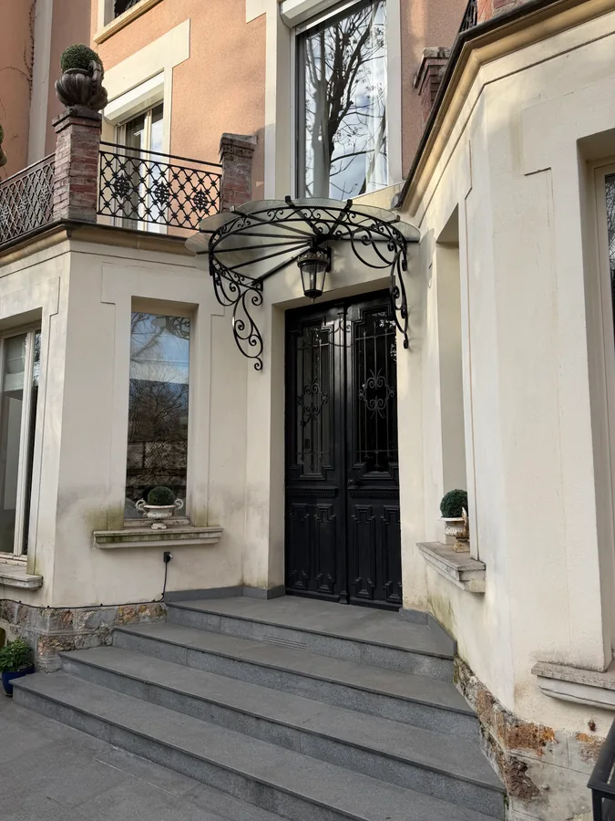 Marquise en fer forgé au-dessus d'une porte d'entrée, façade habillée de verdure, L'Art de Faire