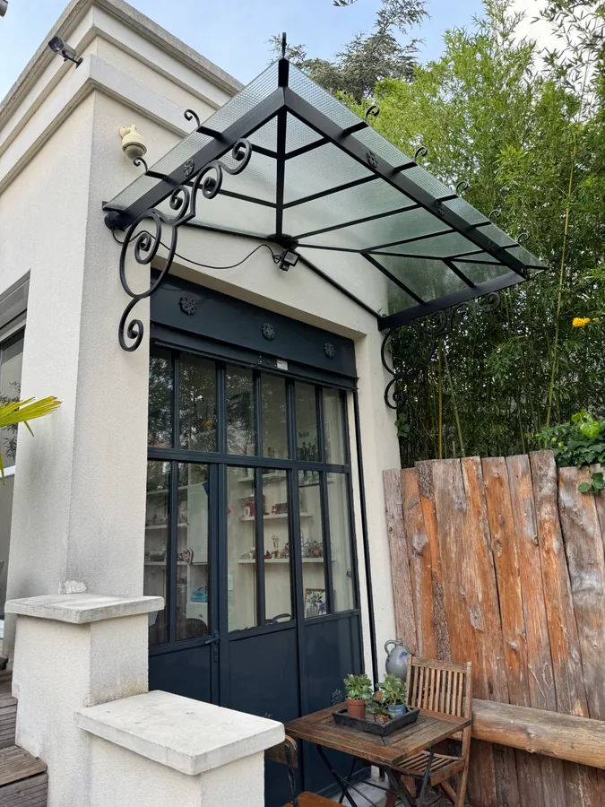 Grand auvent vitré sur ossature fer forgé au-dessus d'une terrasse de jardin, L'Art de Faire