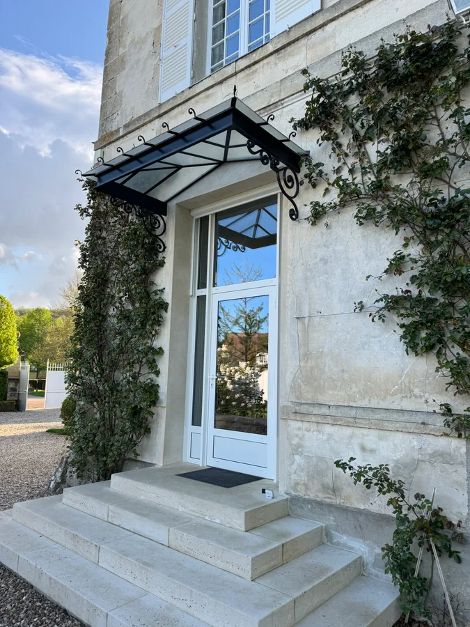Marquise en fer forgé au-dessus d'une entrée, façade claire, L'Art de Faire