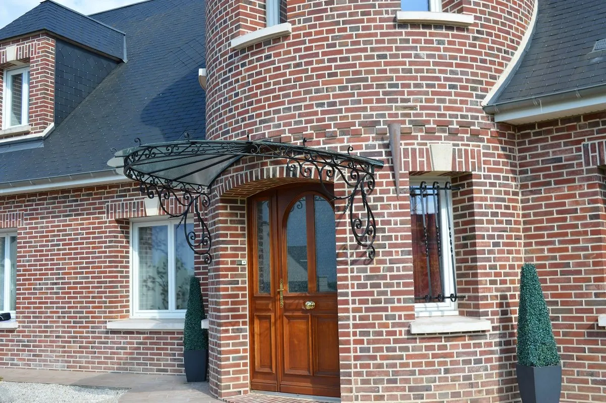 Marquise en fer forgé au-dessus d'une porte en bois, façade en brique, L'Art de Faire