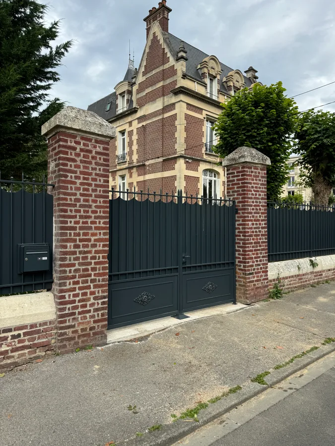Portail en fer forgé noir entre piliers en brique, L'Art de Faire