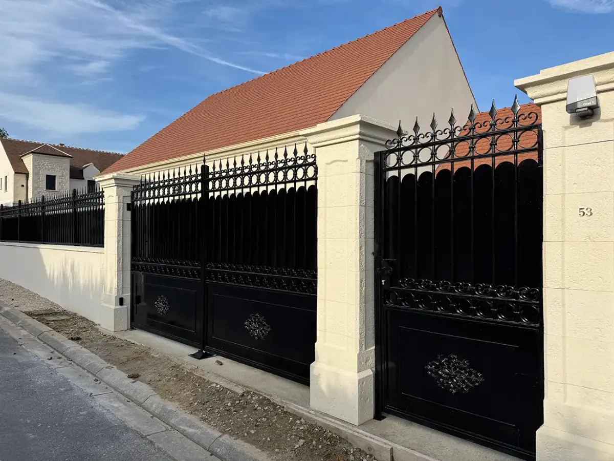 Portail coulissant et clôture en fer forgé noir à barreaux gothiques et médaillon central, piliers en pierre, L'Art de Faire