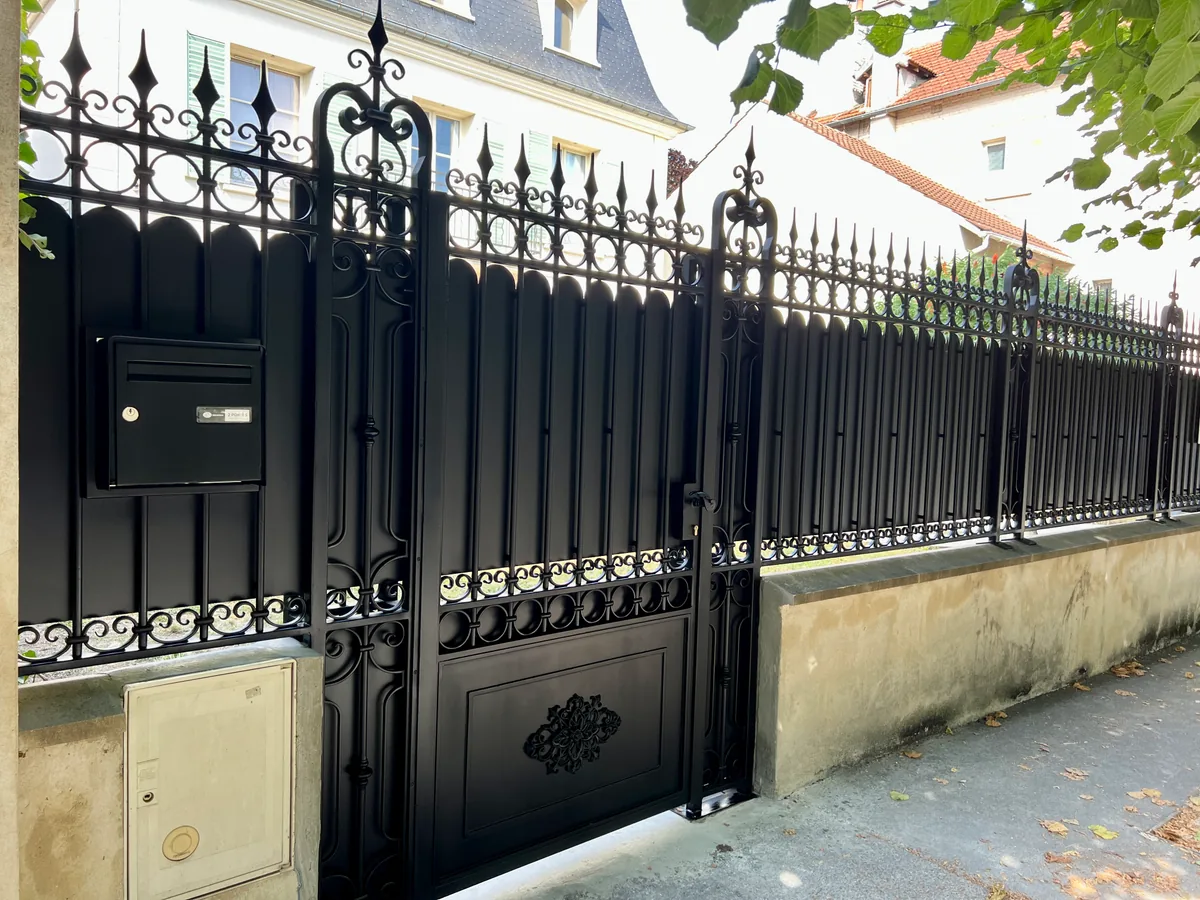Grand portail et clôture en fer forgé noir entre piliers, devant une belle demeure, L'Art de Faire