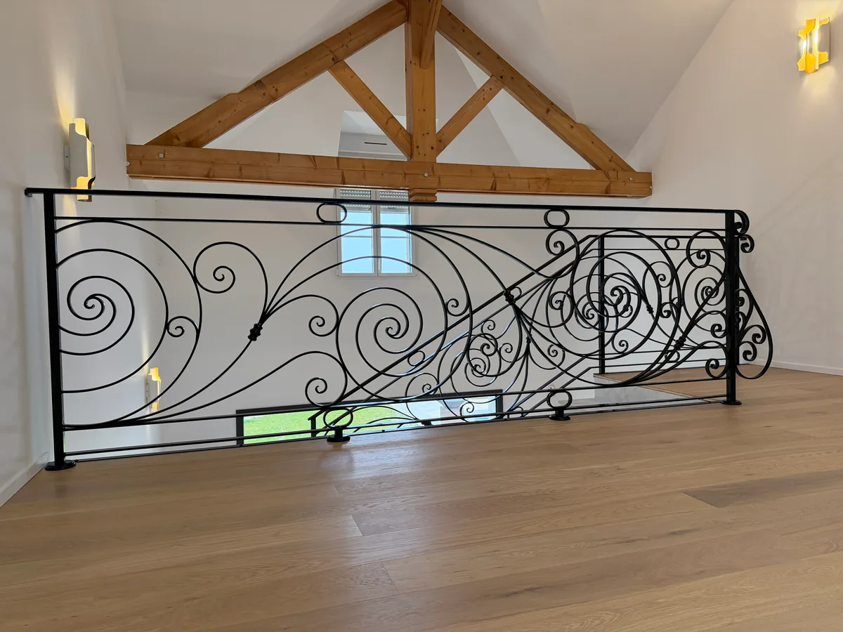 Garde-corps de mezzanine en fer forgé à spirales et volutes sous charpente bois apparente, parquet chêne, L'Art de Faire